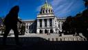 A person is silhouetted in the shade as they walk by the Pennsylvania Capitol in Harrisburg.